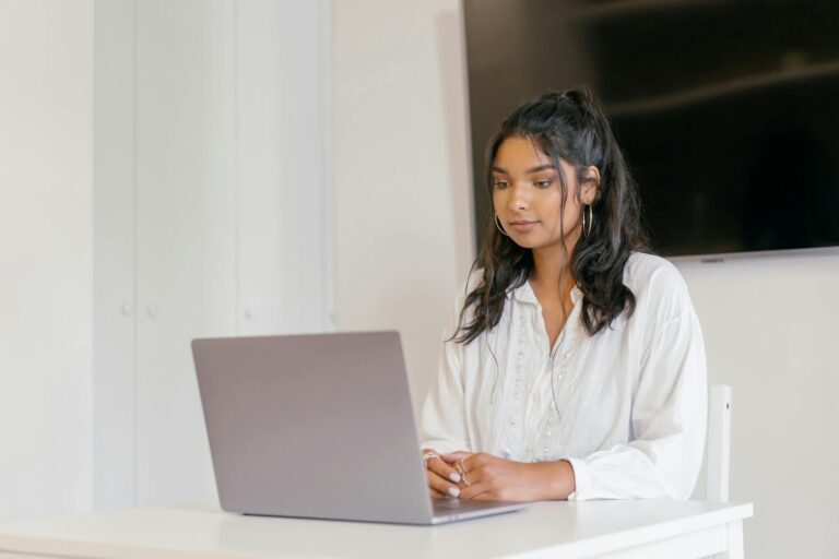 A young woman focused on studying with her laptop in a modern indoor setting.