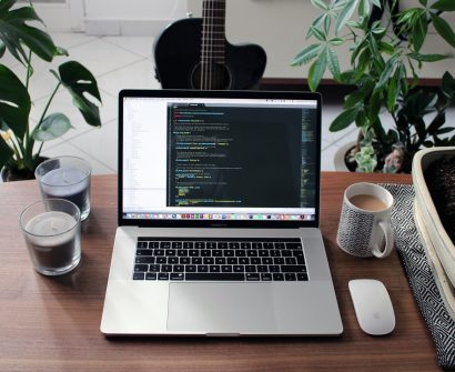 macbook pro beside white ceramic mug on brown wooden table